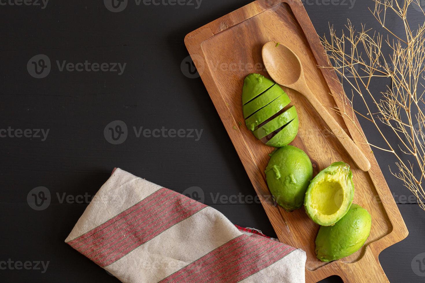 Aguacate orgánico fresco cortado por la mitad sobre una mesa de madera negra foto