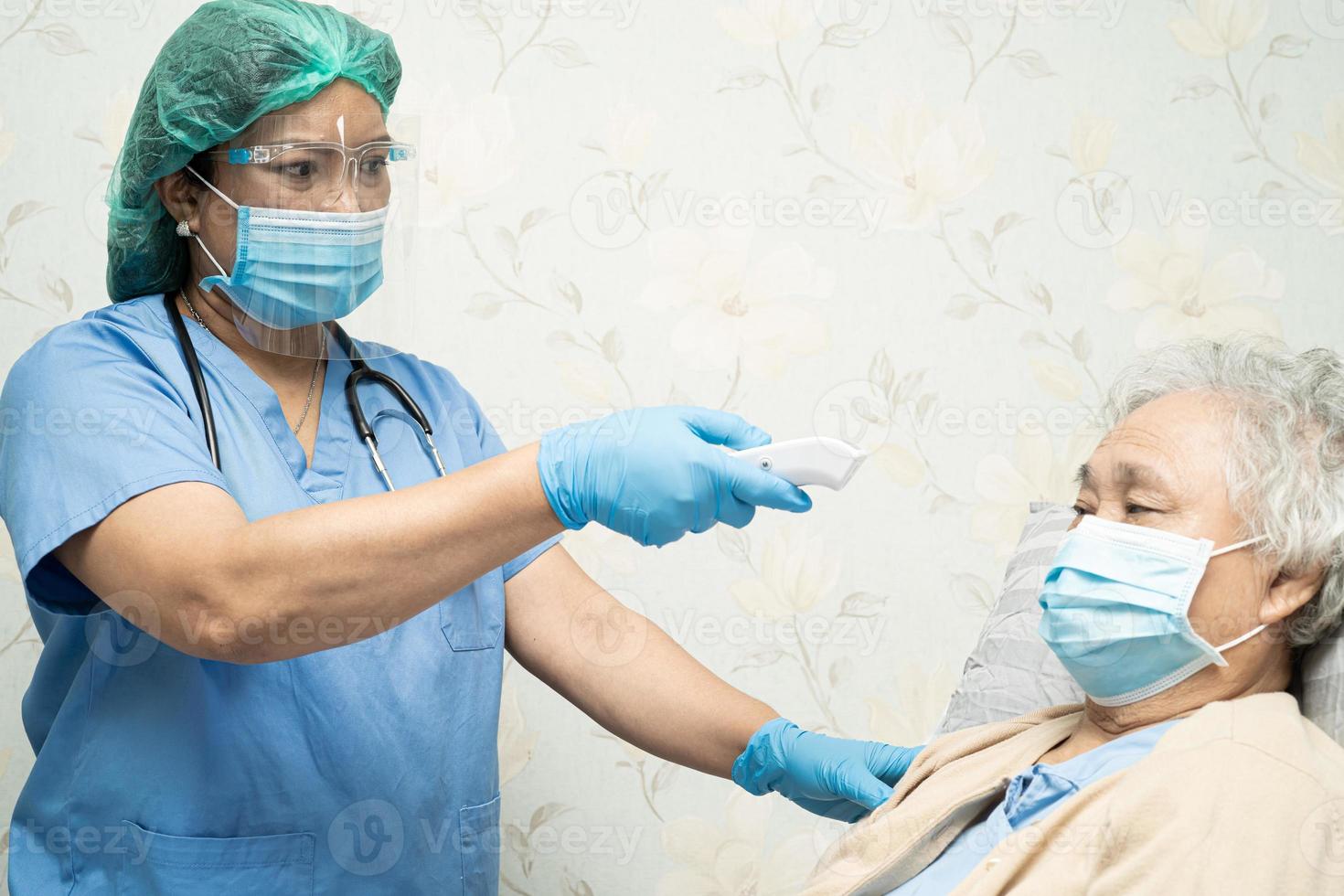 médico asiático con protector facial y traje de ppe nuevo normal para comprobar que el paciente protege la seguridad infección brote de coronavirus covid-19 en la sala de cuarentena del hospital de enfermería. foto
