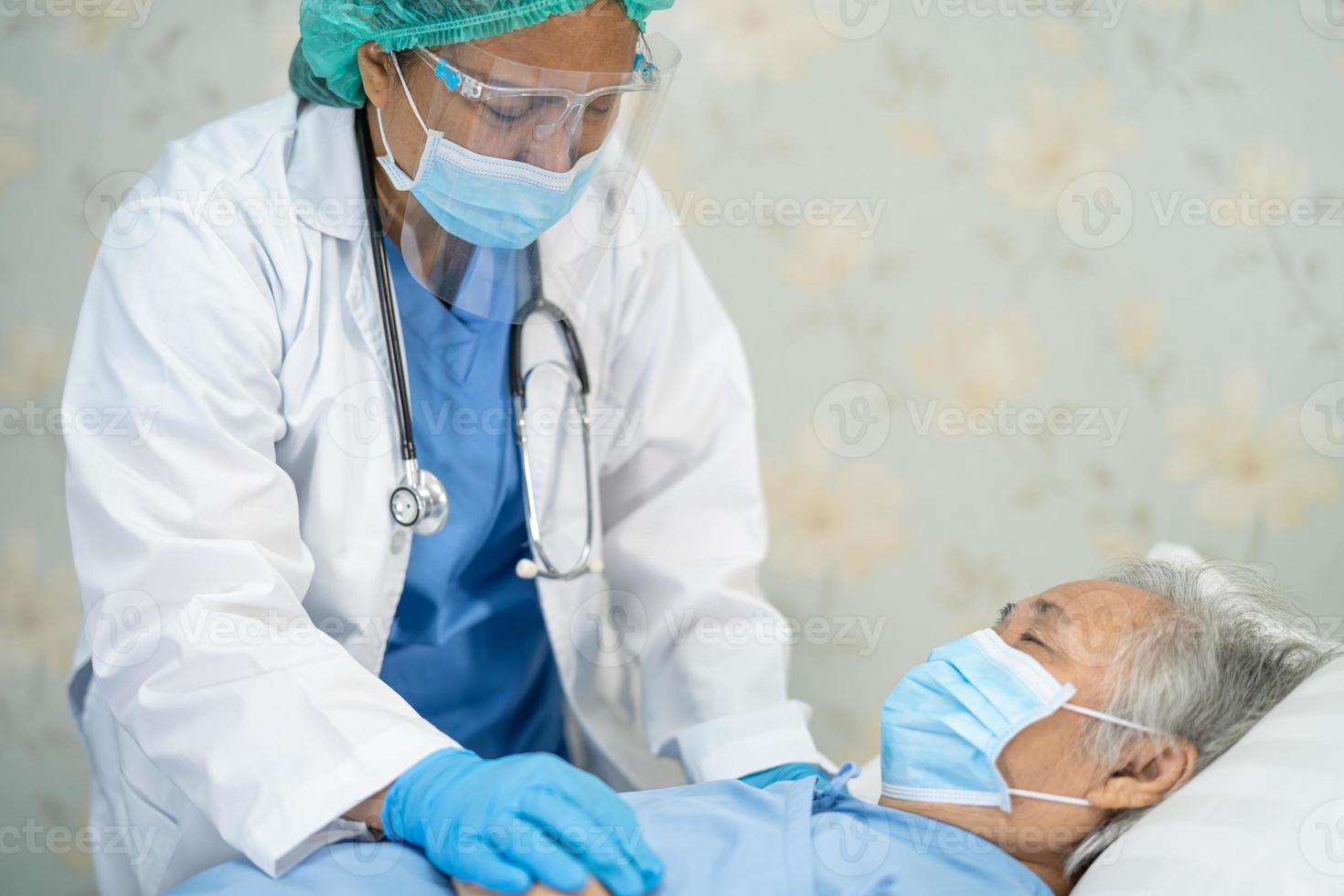 médico asiático con protector facial y traje de ppe nuevo normal para comprobar que el paciente protege la seguridad infección brote de coronavirus covid-19 en la sala de cuarentena del hospital de enfermería. foto