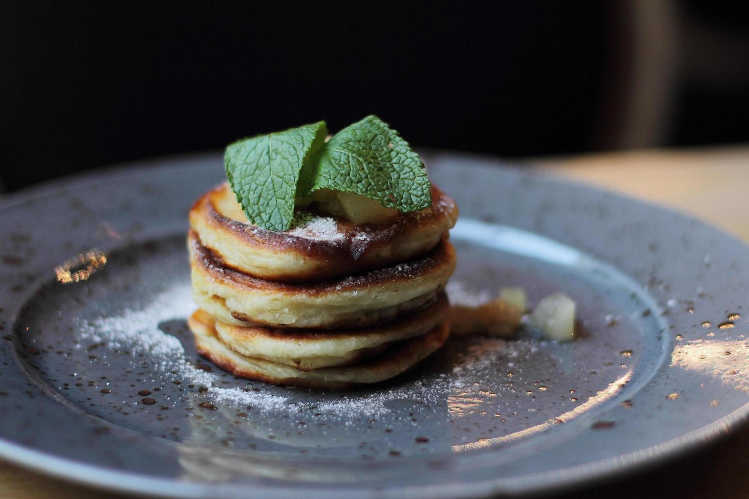 Sabrosos panqueques recién horneados para un desayuno saludable con mermelada de manzana y menta en la placa gris foto