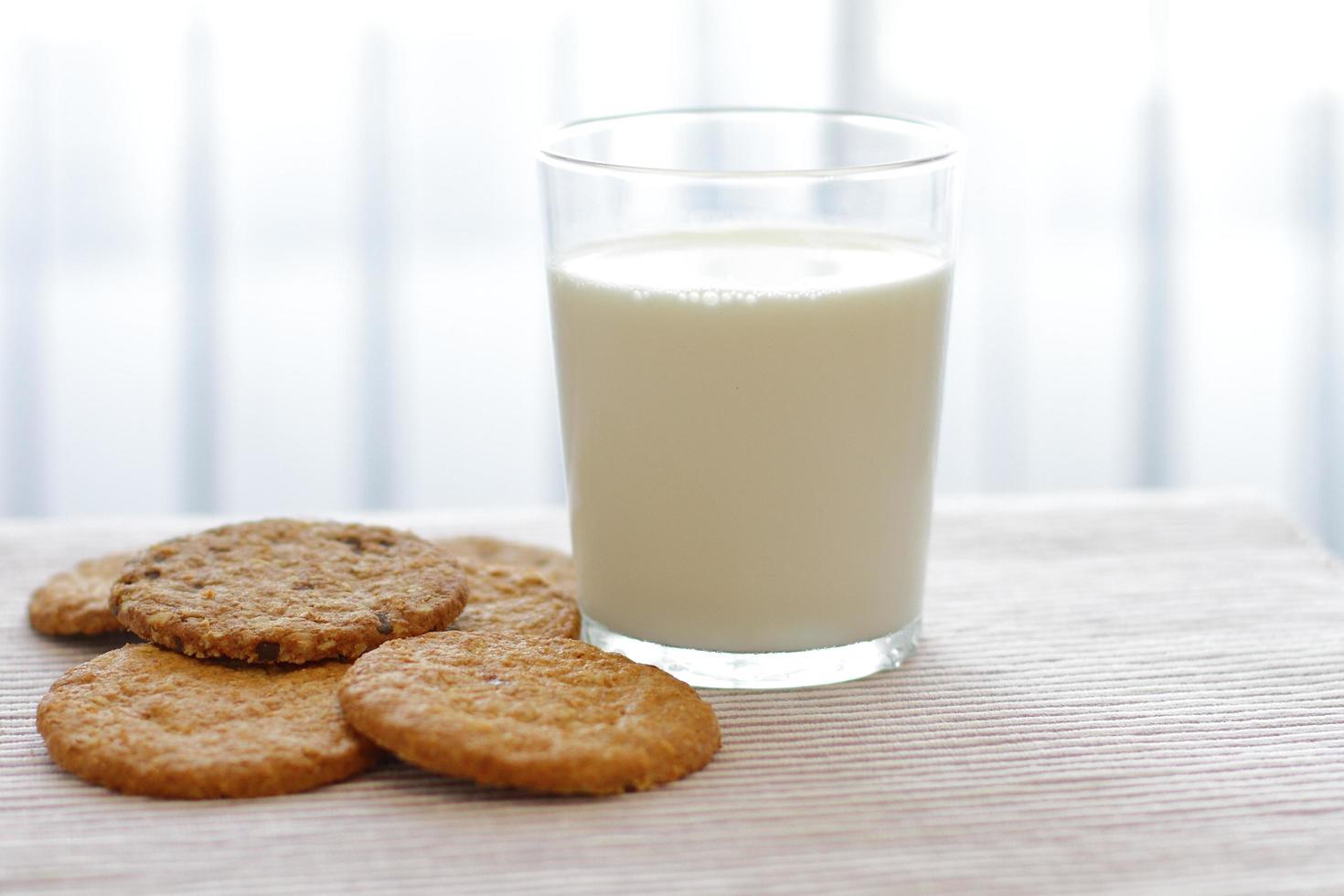 Oat cookies with glass of milk for breakfast on table cloth and blue flower on background, rustic healthy food photo