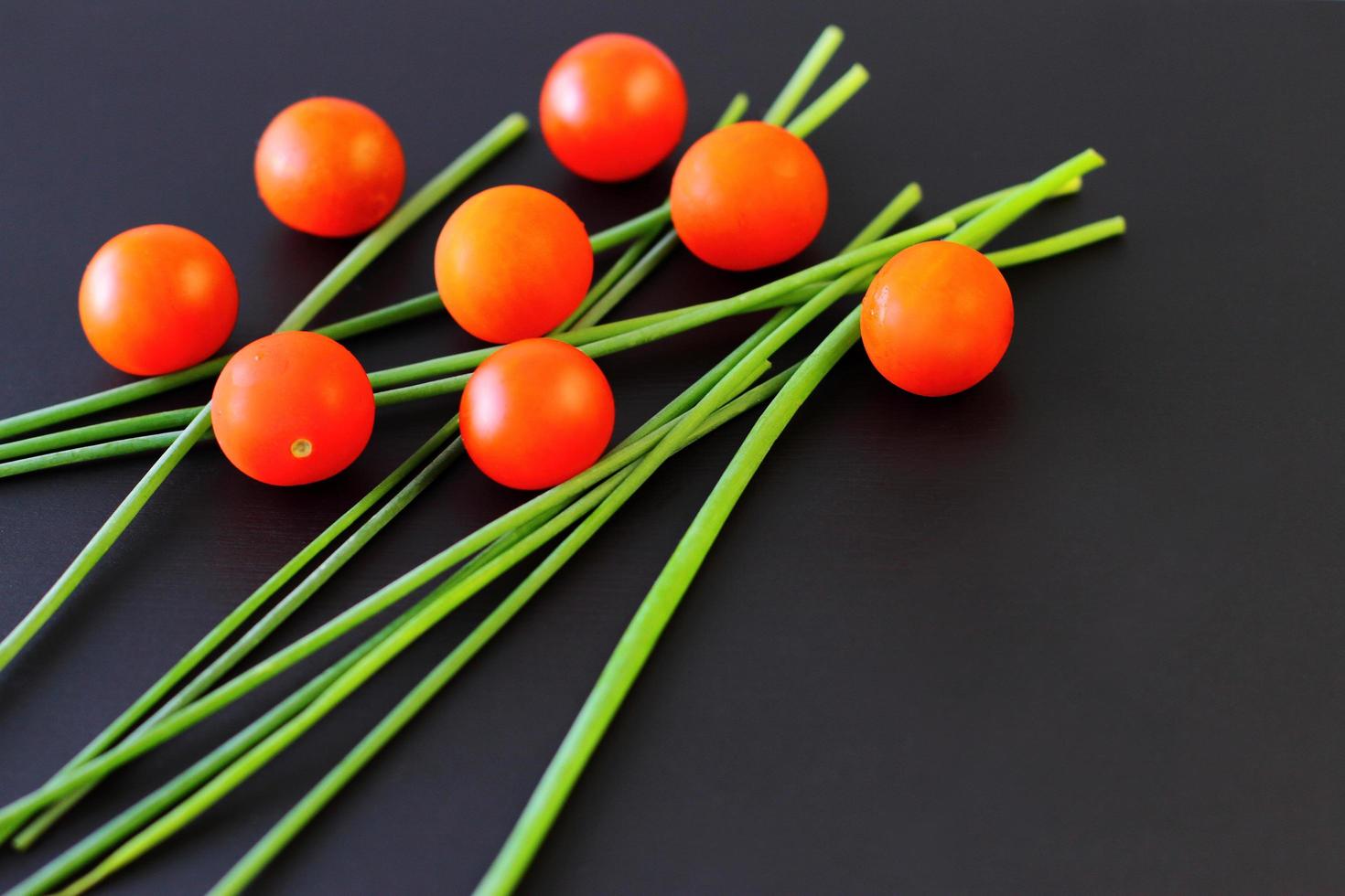 Pequeños tomates cherry rojos y cebolla verde fresca sobre fondo negro rústico, vista superior, espacio de copia foto