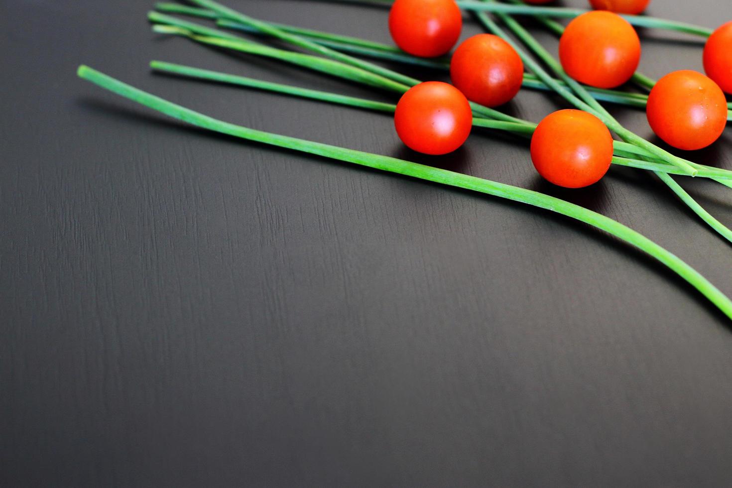 Small red cherry tomatoes and fresh green onion on rustic black background, top view, copy space photo