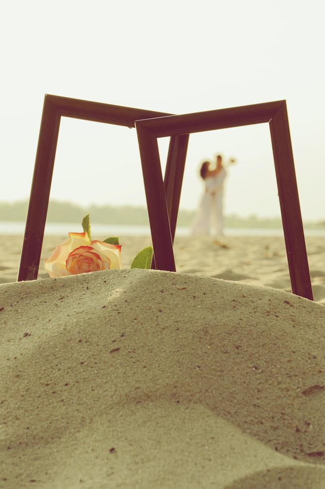 shape of loving just married couple framed on wooden photo frame on sand with rose