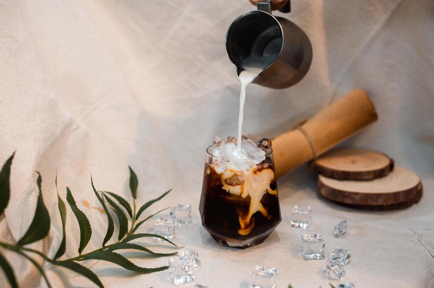 barista vertiendo leche en un vaso de café helado foto