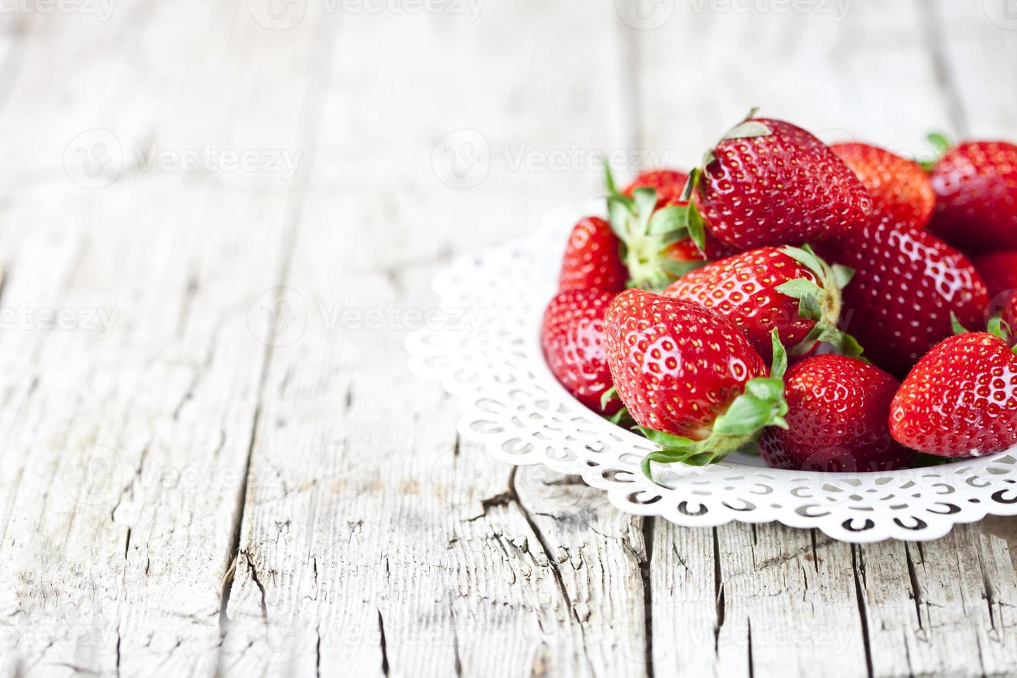 Fresas rojas orgánicas en un plato blanco sobre fondo de madera rústica. alimentos dulces saludables, vitaminas y concepto afrutado. foto