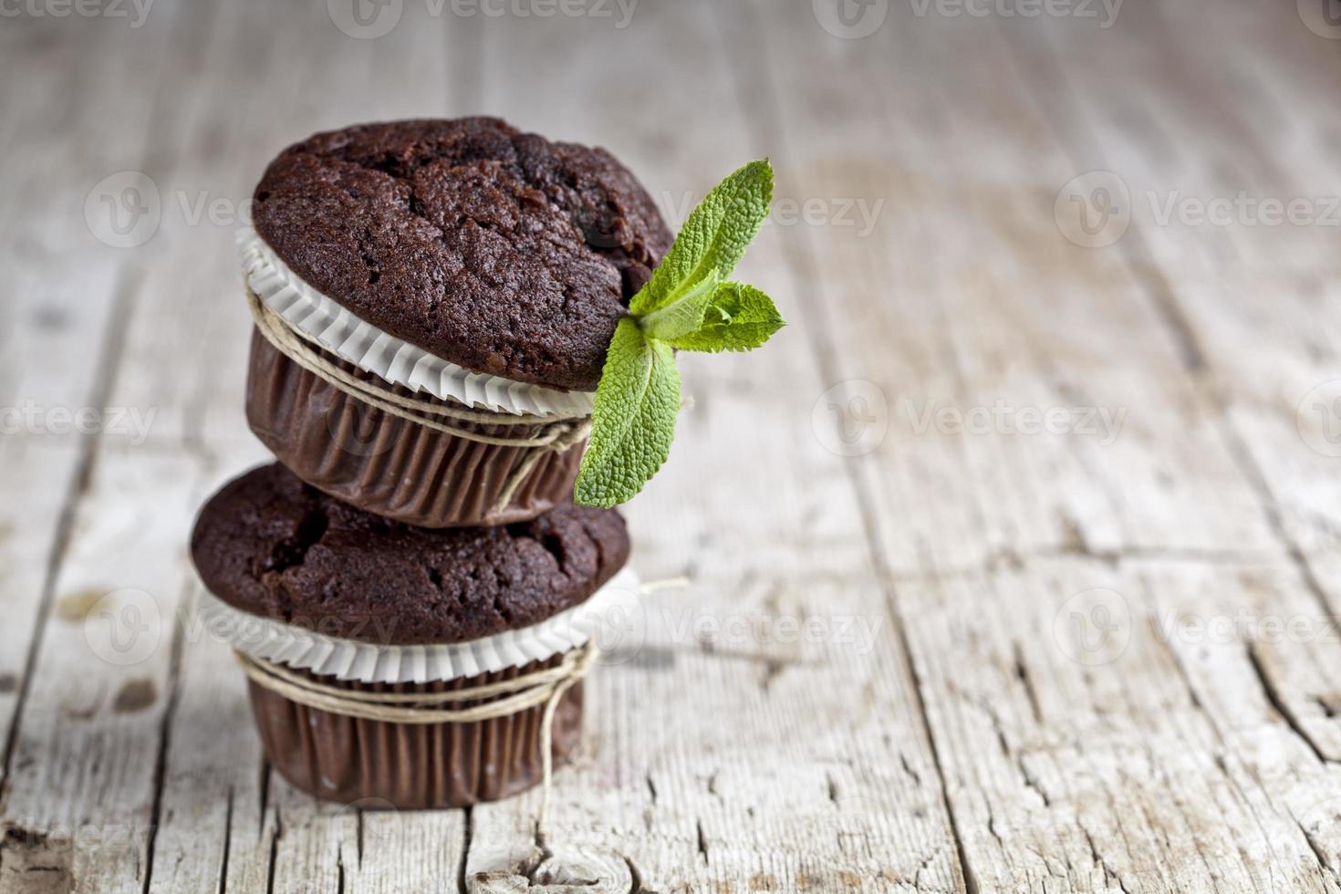 muffins de chocolate oscuro con hojas de menta en la mesa de madera rústica. foto