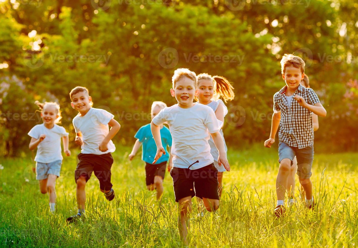 un grupo de niños felices de niños y niñas corren en el parque sobre el césped en un día soleado de verano. foto