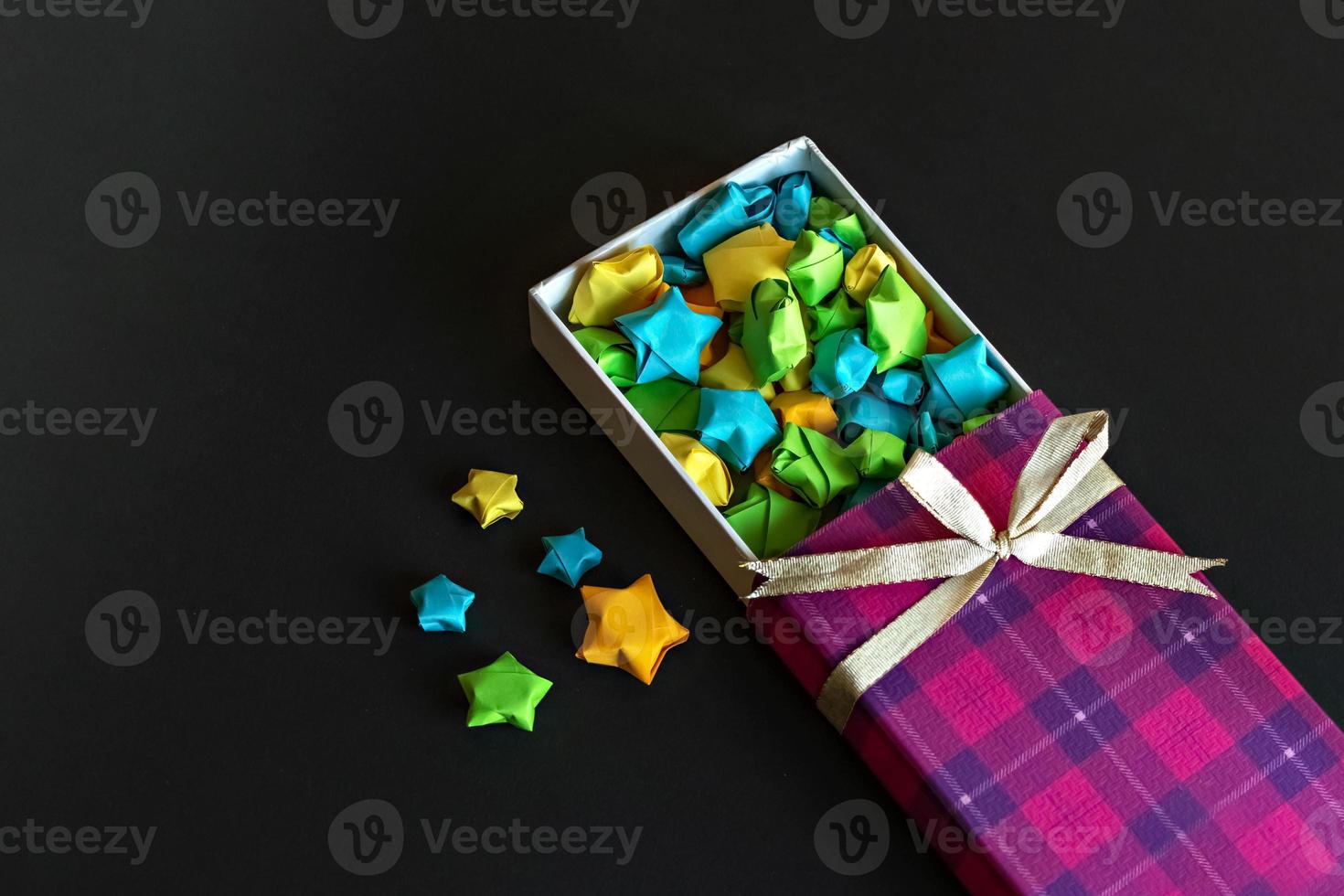 Caja de regalo de color con lazo de raso con estrellas de papel origami sobre fondo negro. regalos para las fiestas. foto