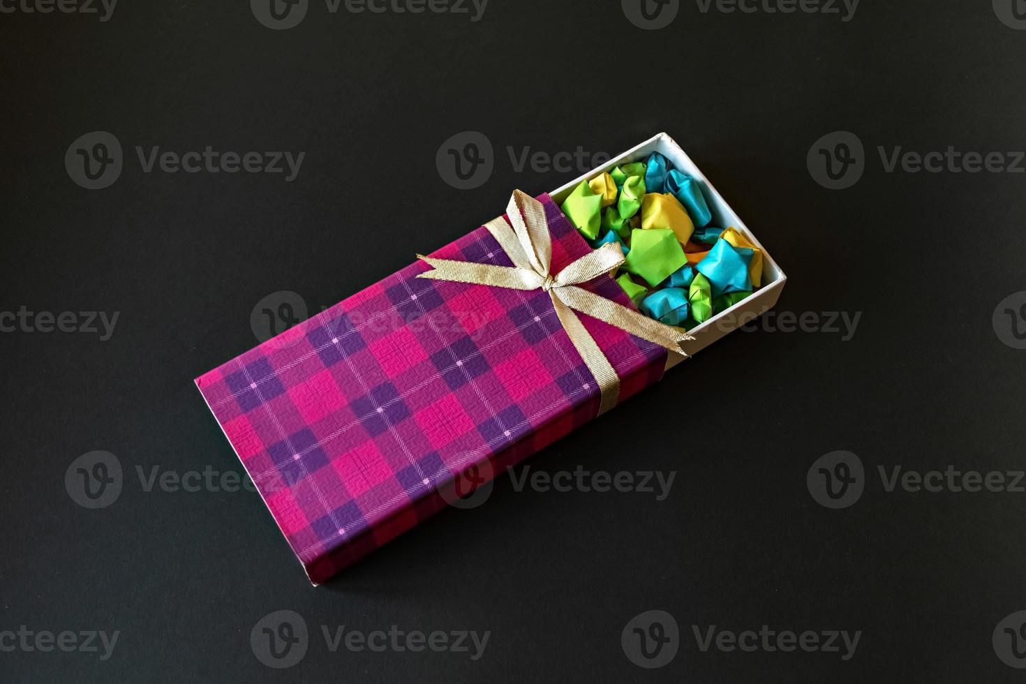 Caja de regalo de color con lazo de raso con estrellas de papel origami sobre fondo negro. regalos para las fiestas. foto