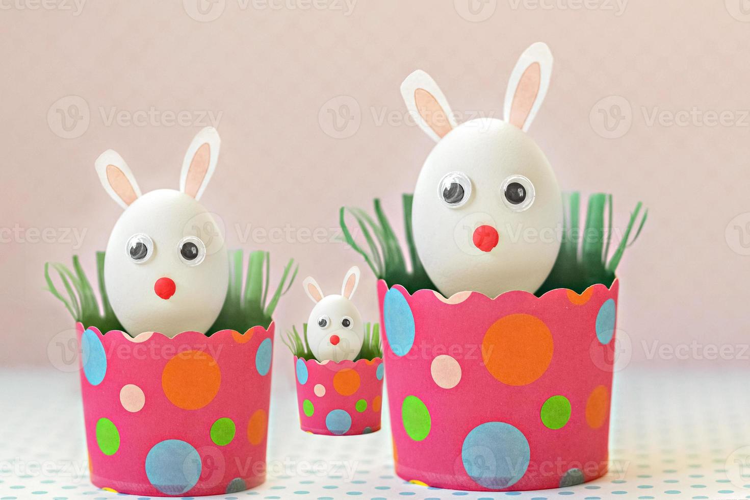 huevos de gallina blanca con orejas de conejo en bandejas de papel rosa ecológicas, cajas. familia feliz concepto de vacaciones de pascua. foto