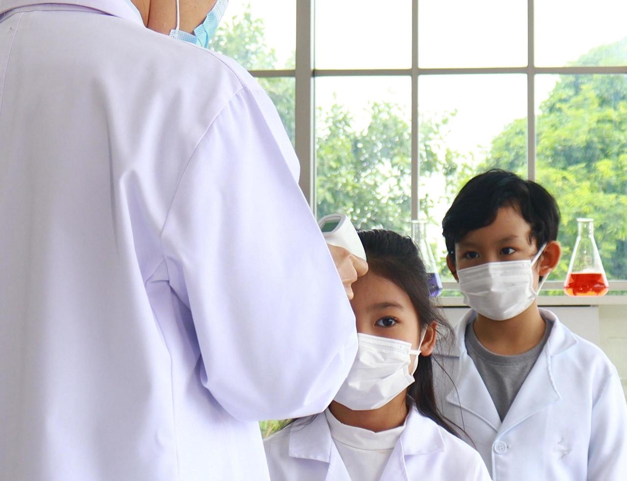 Teacher pointed an electronic gun thermometer to his forehead to measure the body temperature of the students photo