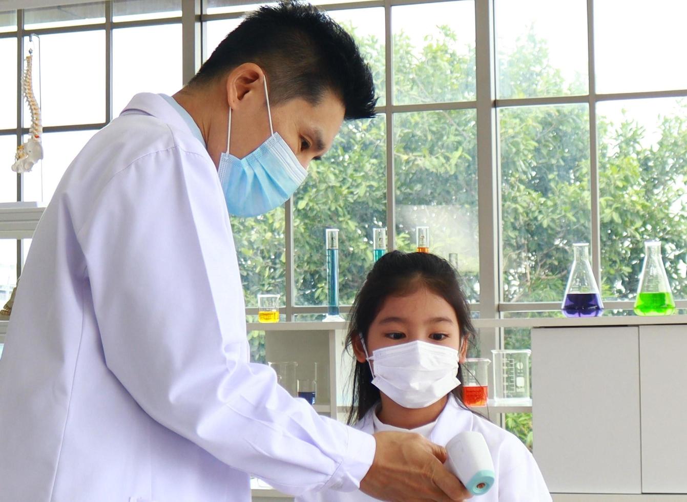 Teachers are using an infrared forehead thermometer to check the temperature of a male student before going to class for symptoms of COVID-19. Concept of epidemic prevention photo