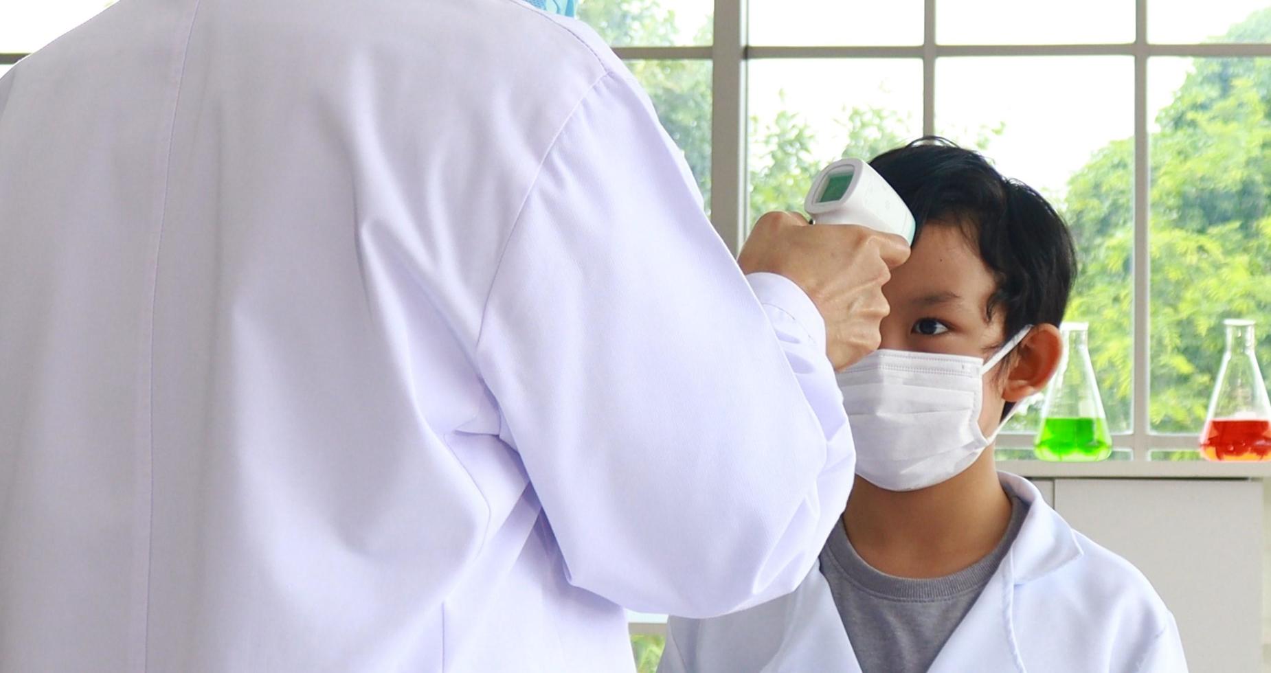 Teachers are using an infrared forehead thermometer to check the temperature of a male student before going to class for symptoms of COVID-19. Concept of epidemic prevention photo