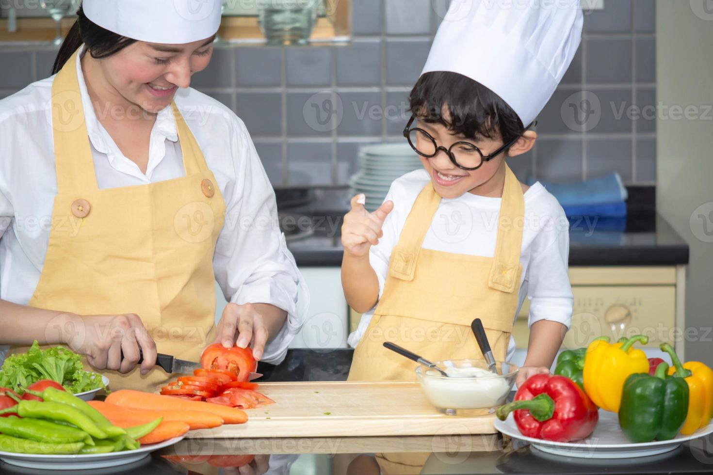 Asian woman young mother with son boy cooking salad food with vegetable holding tomatoes and carrots, bell peppers on plate for happy family cook food enjoyment lifestyle kitchen in home photo