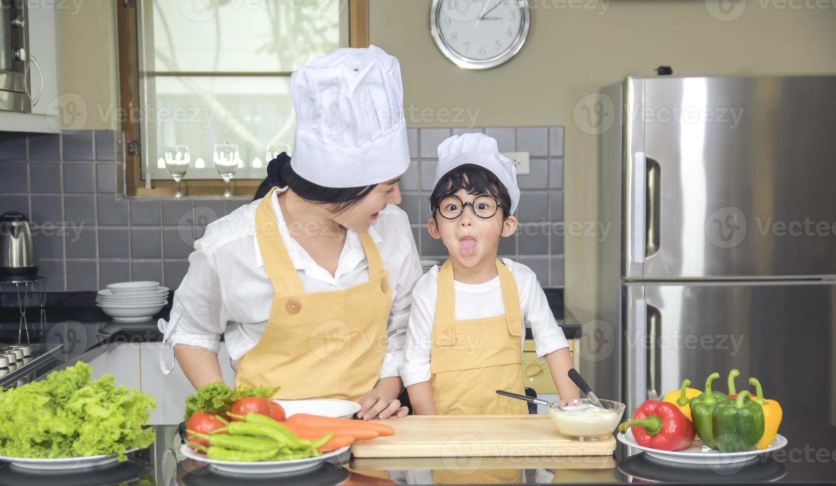 Asian woman young mother with son boy cooking salad food with vegetable holding tomatoes and carrots, bell peppers on plate for happy family cook food enjoyment lifestyle kitchen in home photo