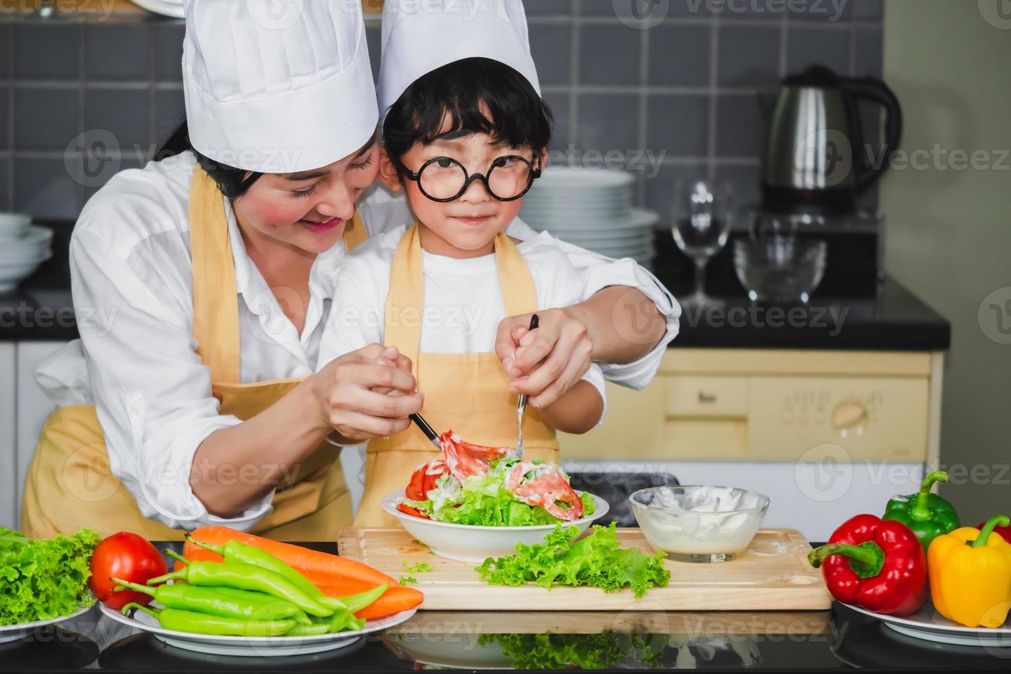 mujer asiática joven madre con hijo niño cocinando ensalada mamá verduras en rodajas comida hijo degustación aderezo de ensalada vegetales zanahorias y tomates pimientos familia feliz cocinar comida disfrute estilo de vida cocina foto