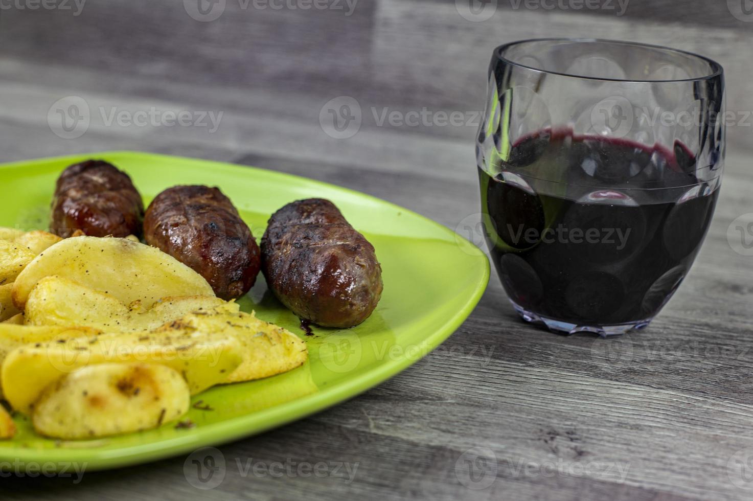 plato salchichas patatas y una copa de vino foto