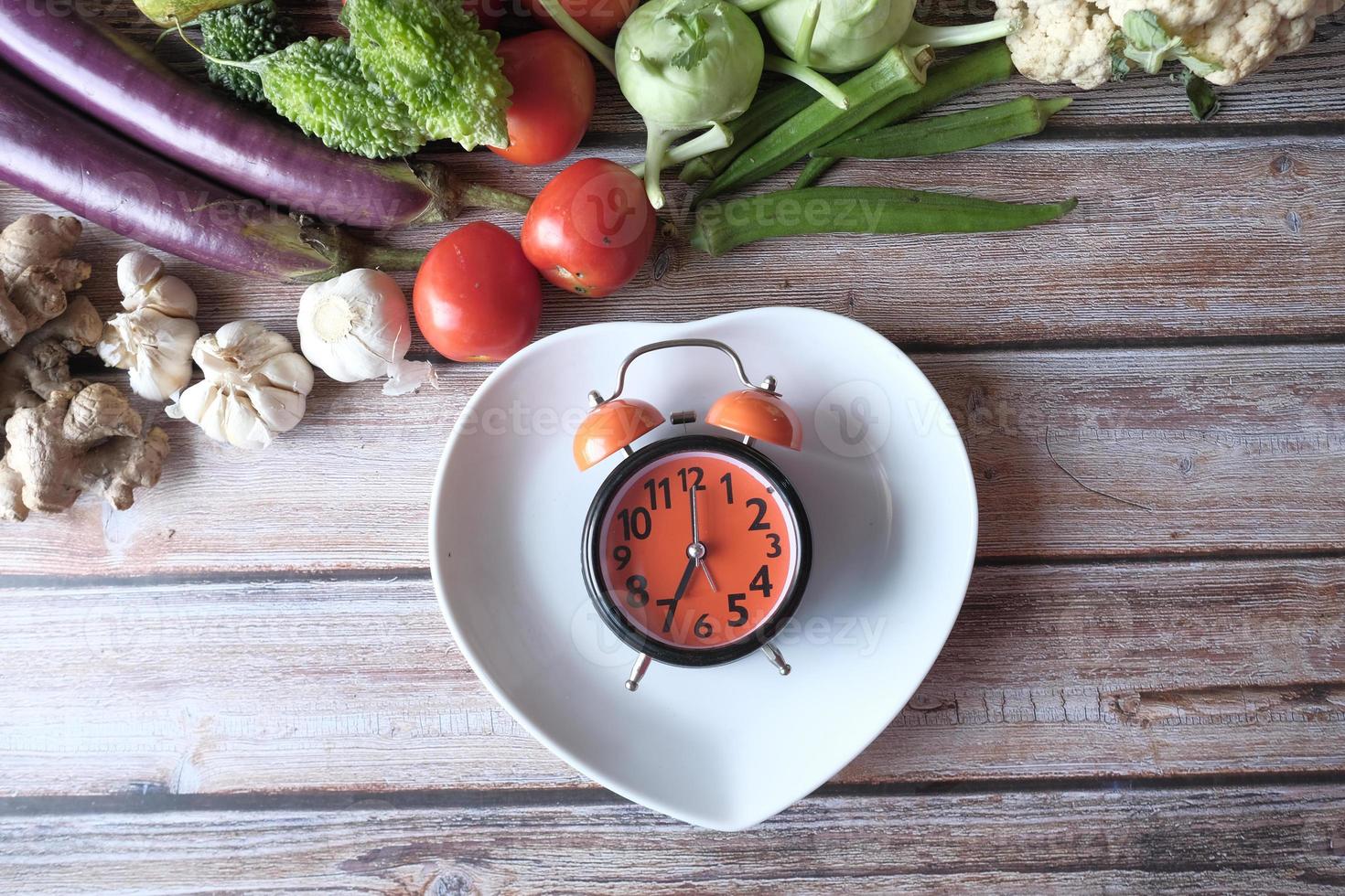 Selección de alimentos saludables con verduras frescas y reloj despertador en la placa foto