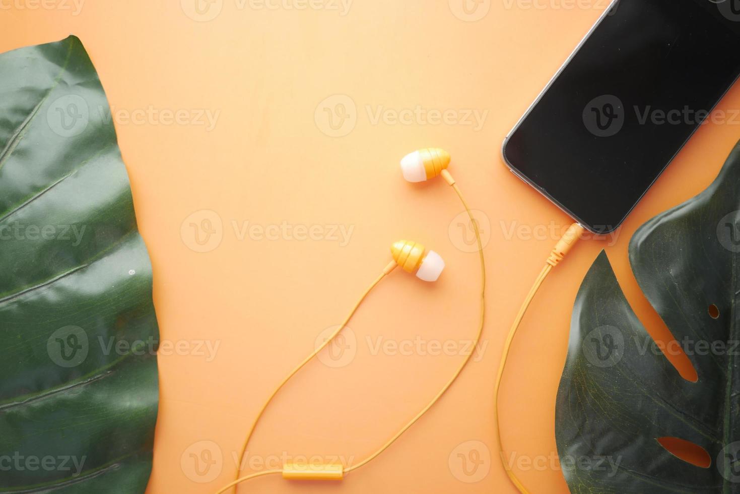 Smart phone with empty screen, earphone on orange background photo