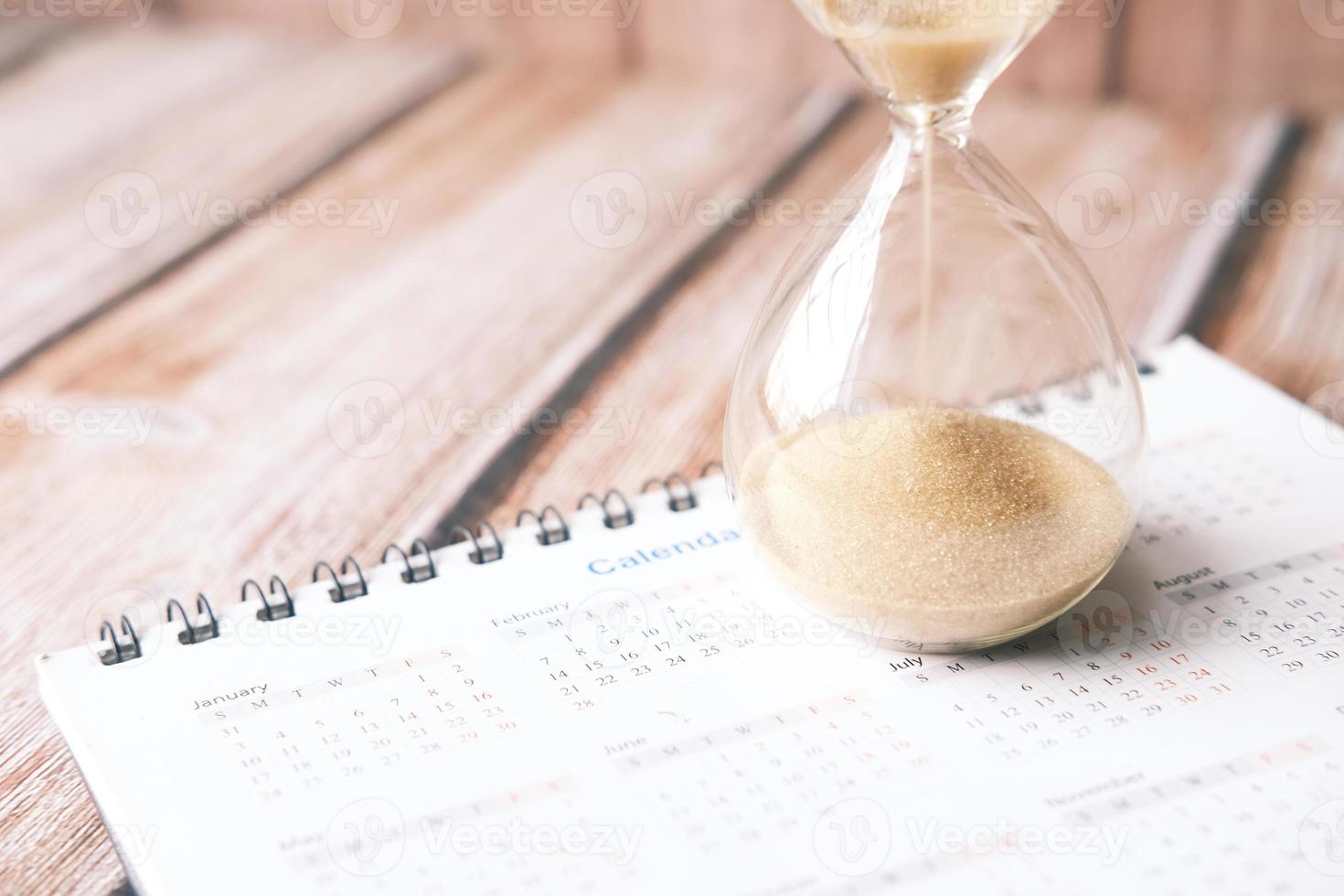 hourglass on calendar on table, sand flowing through the bulb of sandglass photo