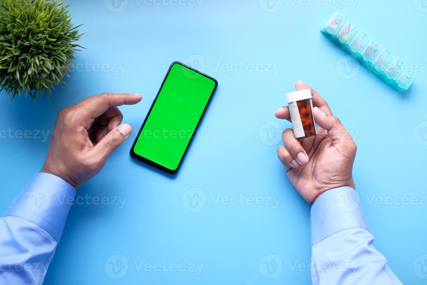 Top view of young man hand using smart phone and holding a pill container photo