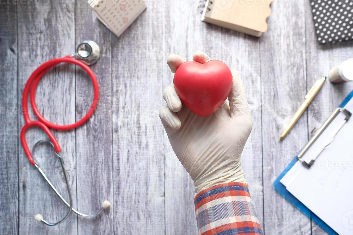 Mano en guantes protectores sosteniendo corazón rojo sobre azul foto