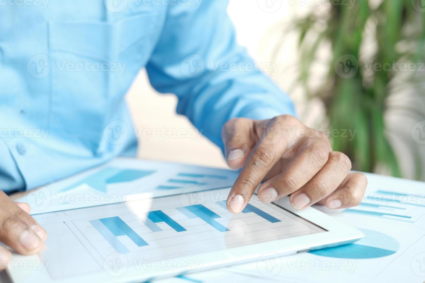 Man's hand working on digital tablet at office desk, using self created chart photo