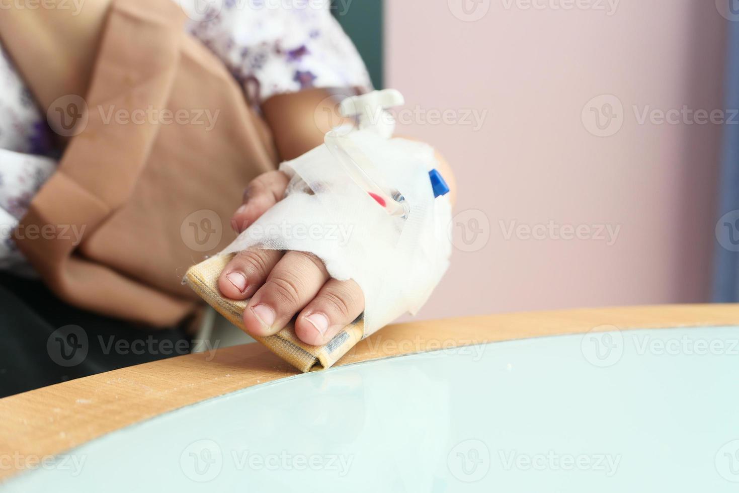 Mano de bebé con vendaje dando solución salina en la cama de un hospital foto