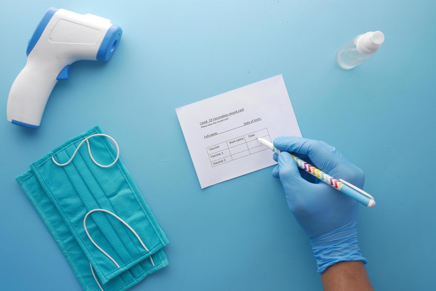 Vaccination record card , hand sanitizer and mask on color background photo