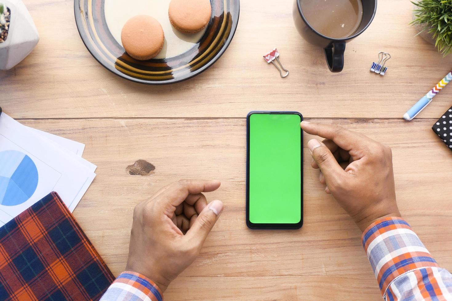 Vista superior de la mano del hombre con un teléfono inteligente en el escritorio de la oficina foto