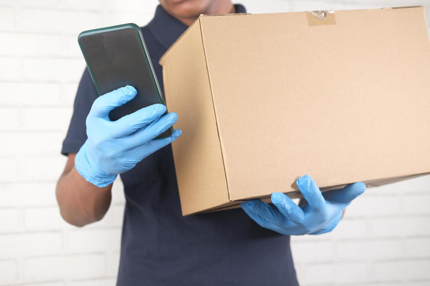 Delivery man hand in latex gloves holding smart phone and card box photo