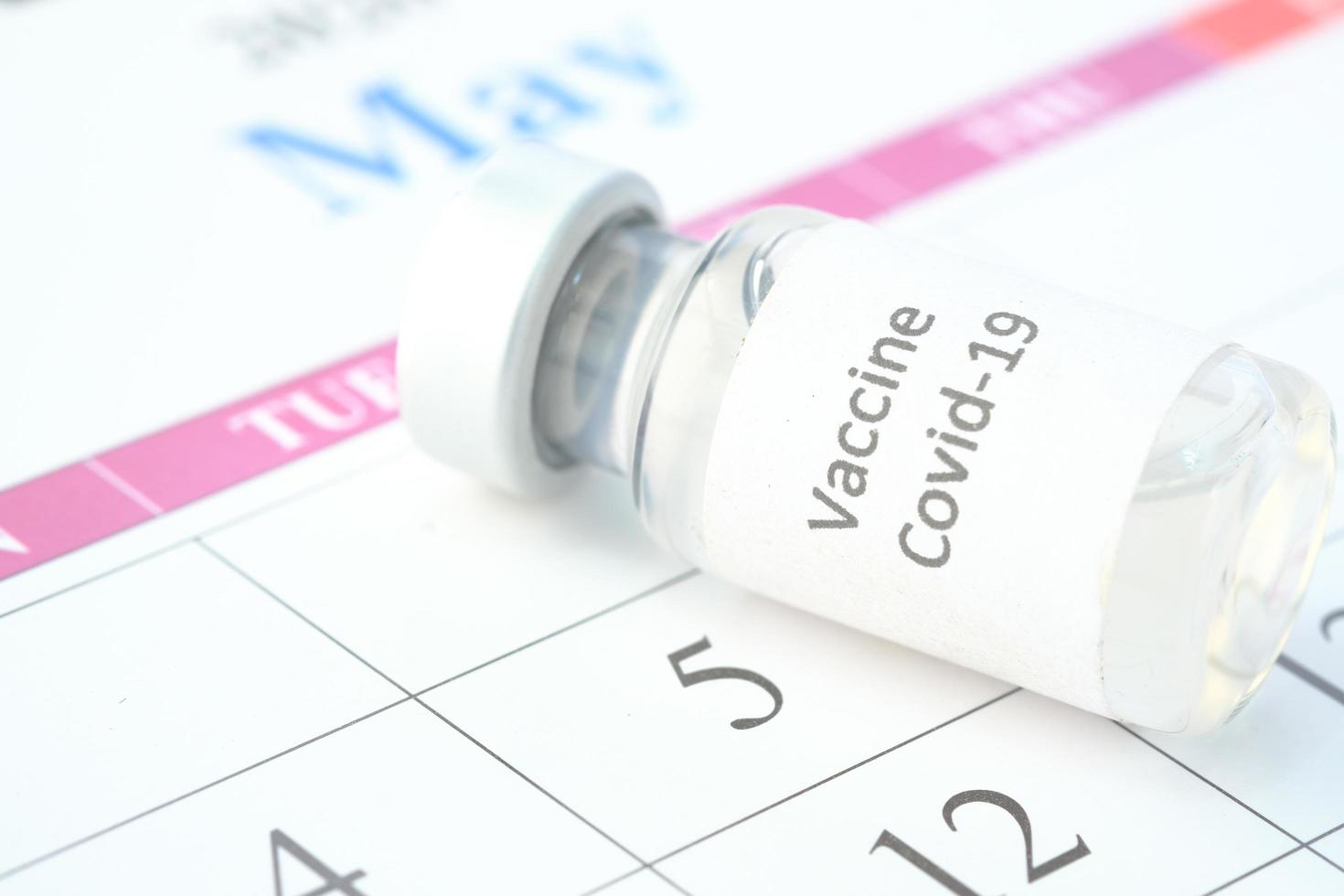 Concepto del día de la vacuna ampolla de vidrio con vacuna y jeringa en el calendario foto