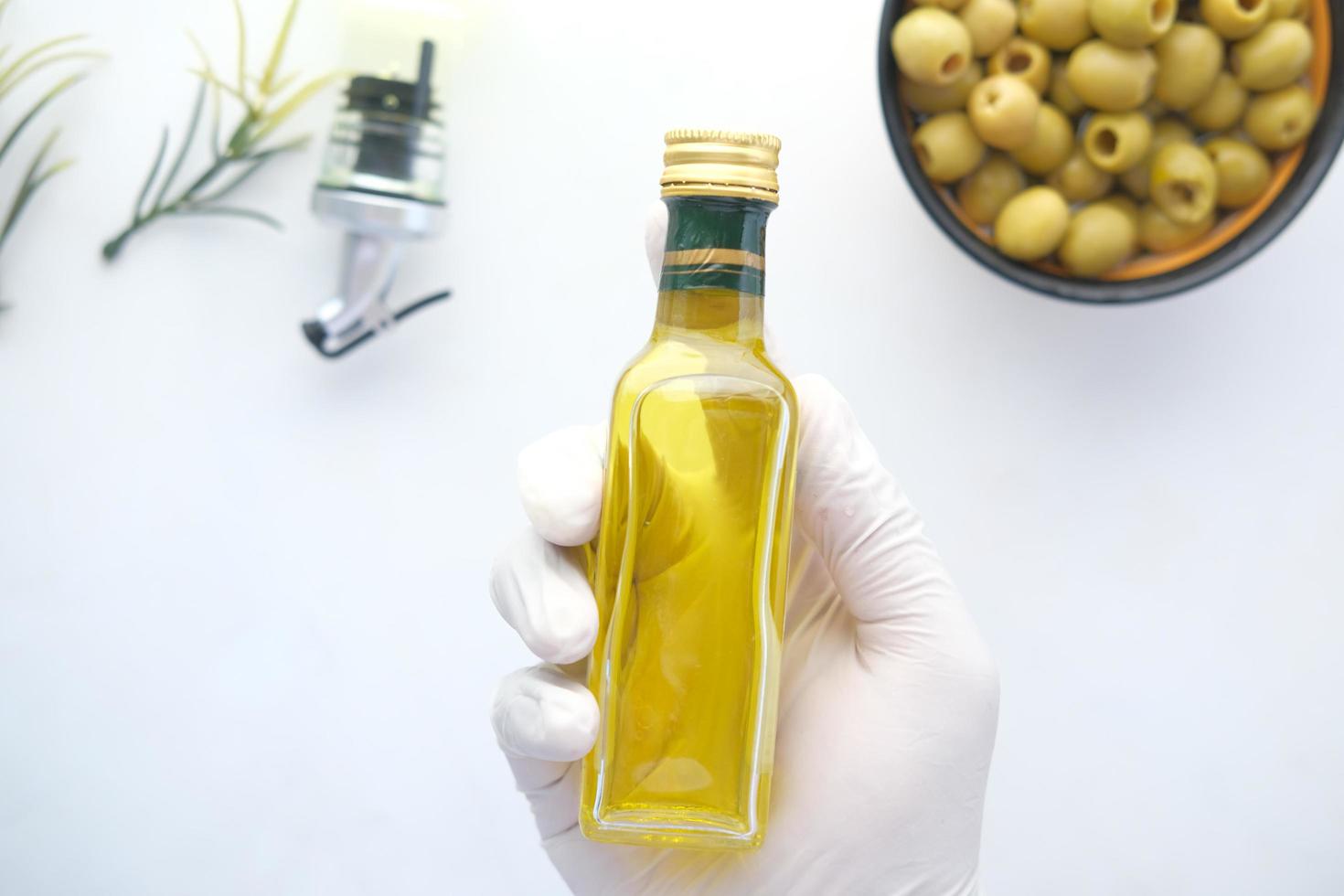 Holding bottle of olive oil and fresh olive in a container on white . photo