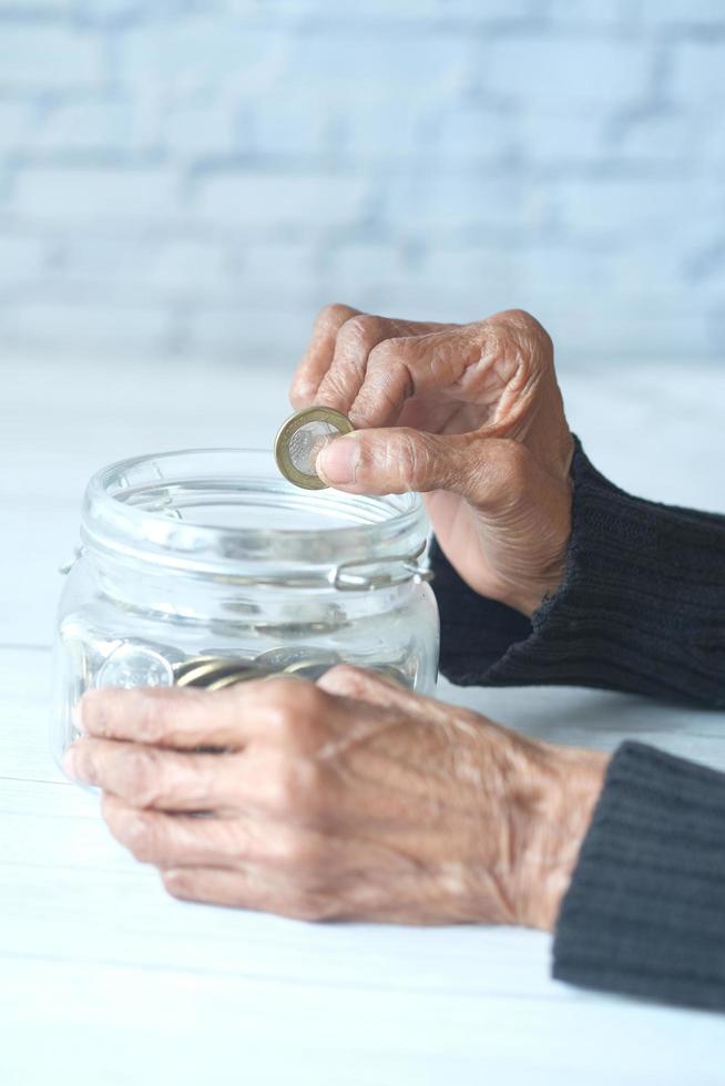 Side view of senior women hand saving coins in a jar photo