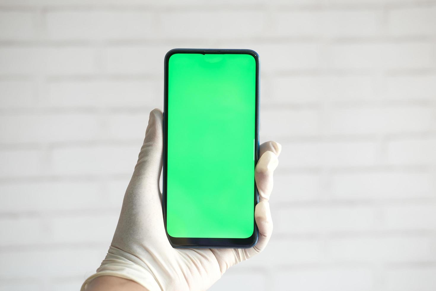 Mano en guantes de látex sosteniendo un teléfono inteligente con pantalla verde foto