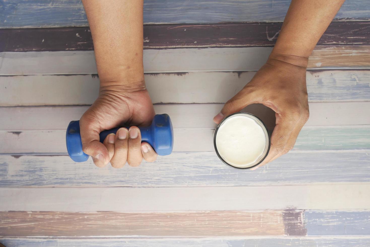 Mano de hombre joven haciendo ejercicio con pesas y sosteniendo un vaso de leche foto