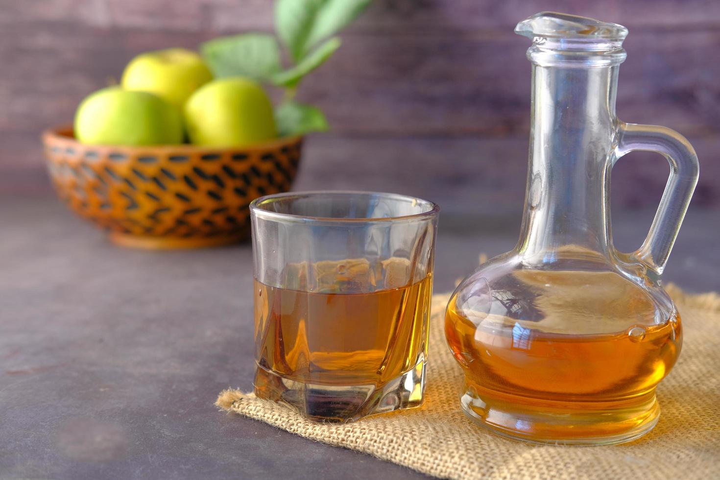 Vinagre de manzana en botella de vidrio con manzana verde fresca en la mesa foto