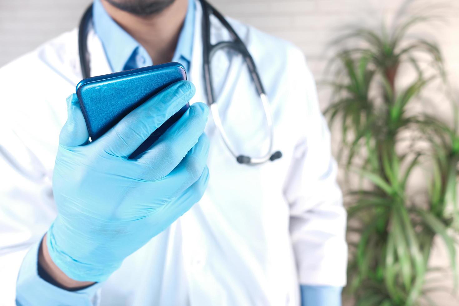 La mano de soctor en guantes protectores con un teléfono inteligente. foto