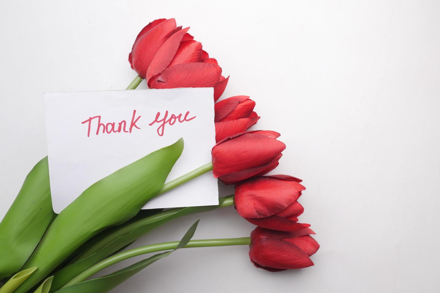 Mensaje de agradecimiento en papel con flor de tulipán sobre fondo blanco. foto