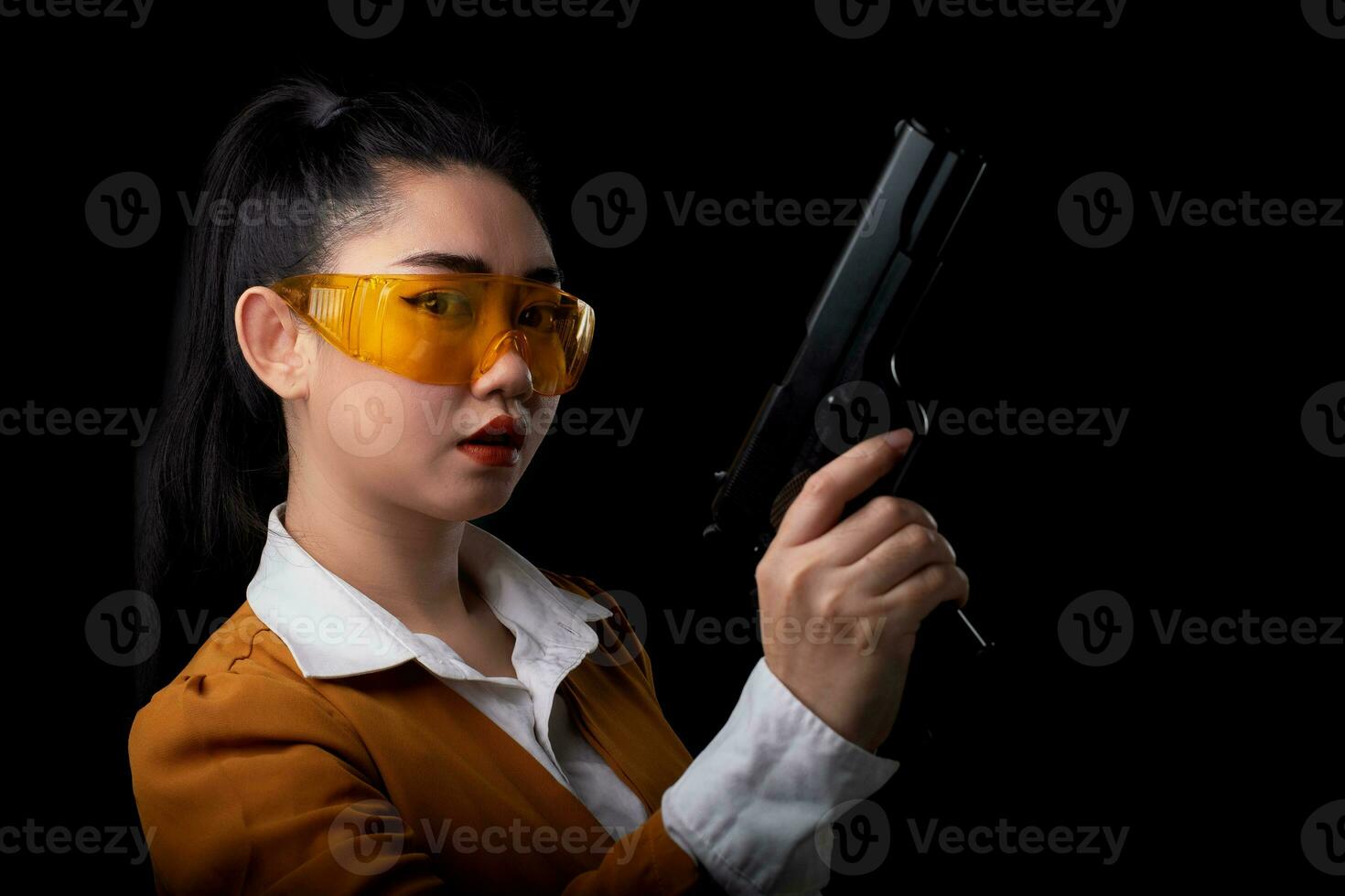 Retrato hermosa mujer asiática vistiendo un traje amarillo con una mano sosteniendo la pistola en el fondo negro foto