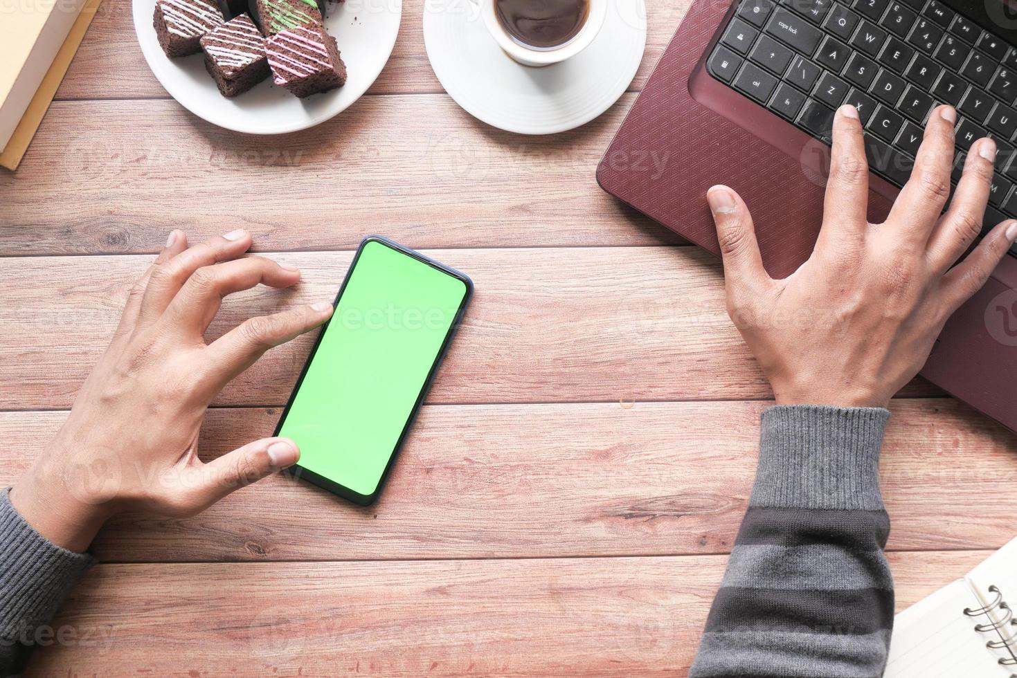 Top view of man hand using smart phone and typing on laptop photo