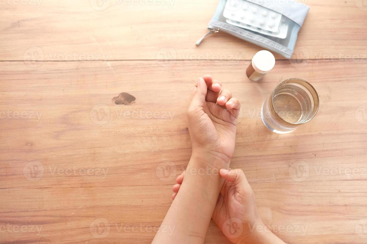 Manos de mujeres jóvenes que sufren dolor de muñeca con píldoras médicas en la mesa foto