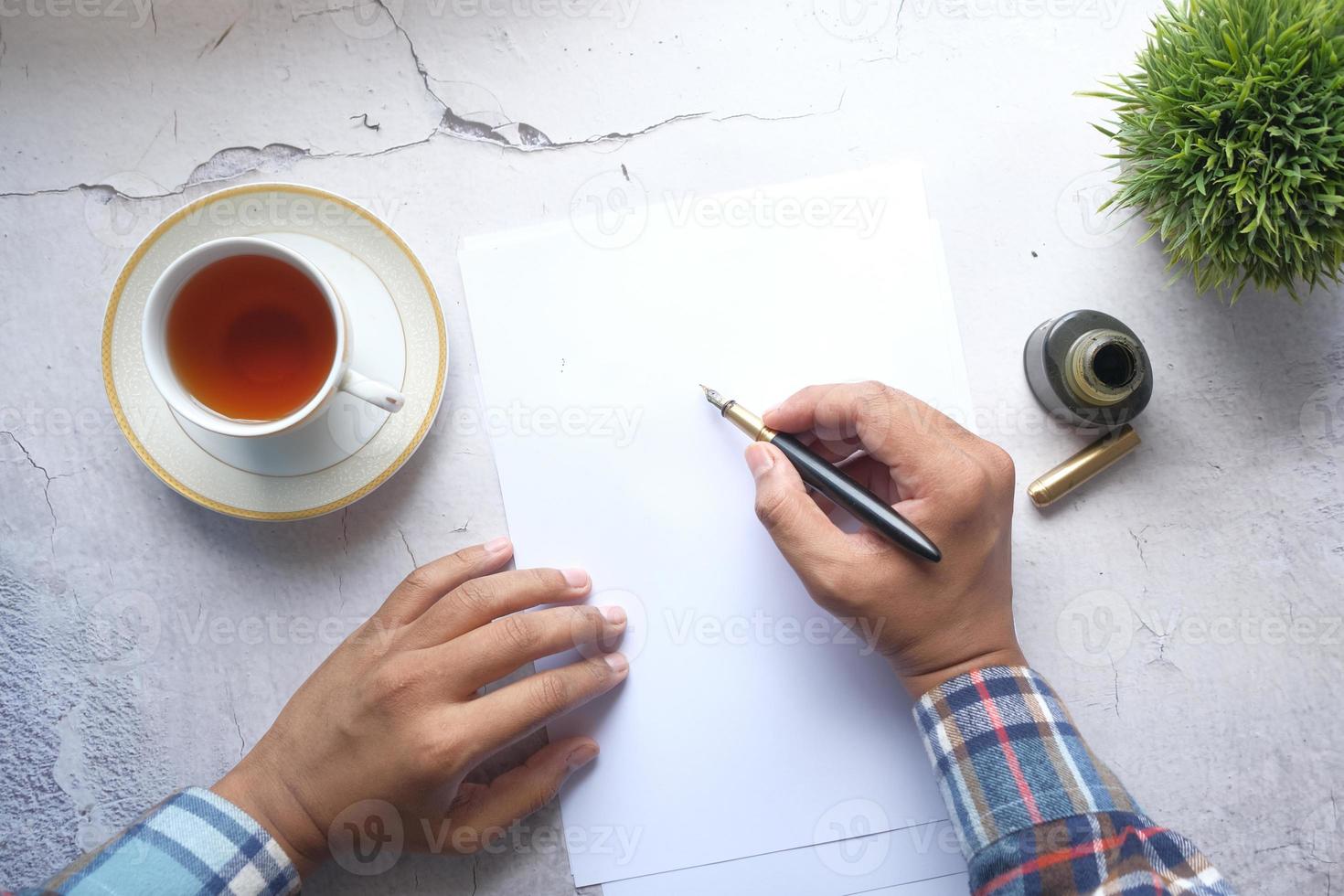 Escritura a mano joven con pluma estilográfica sobre un papel sobre la mesa foto