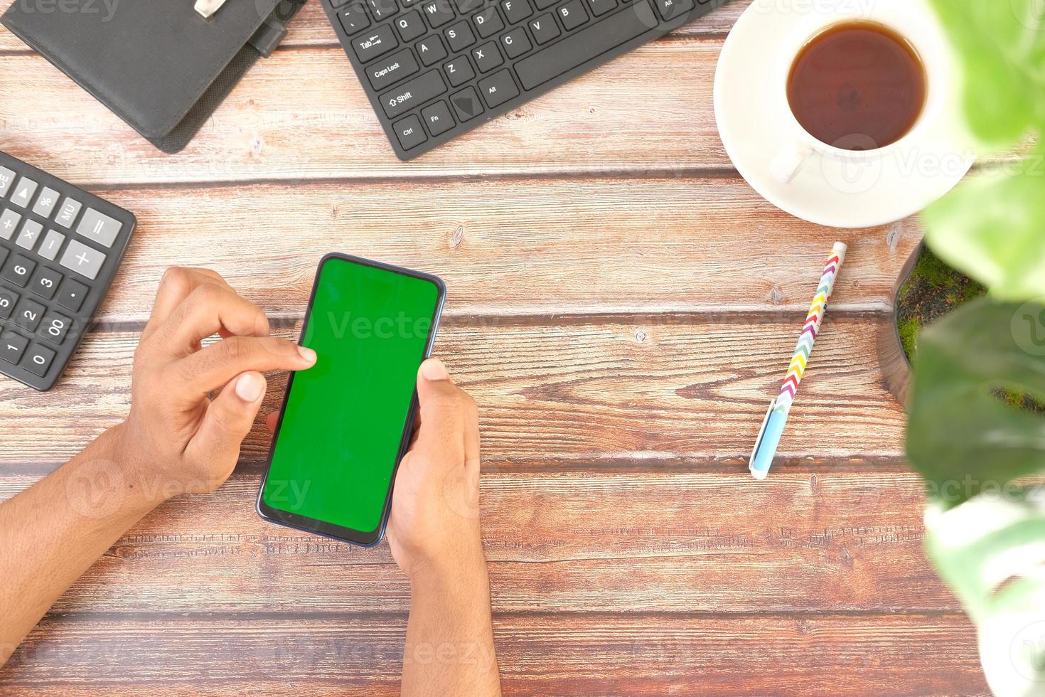 Vista superior de la mano del hombre con un teléfono inteligente en el escritorio de la oficina foto