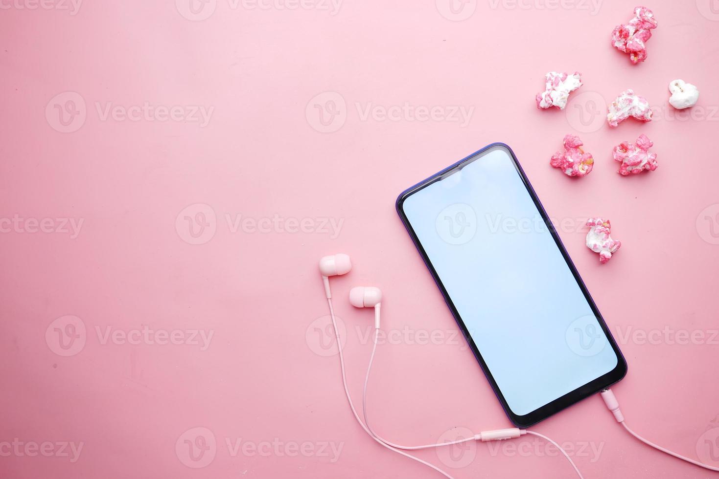 Top view of smart phone, ear phone and popcorn on pink photo