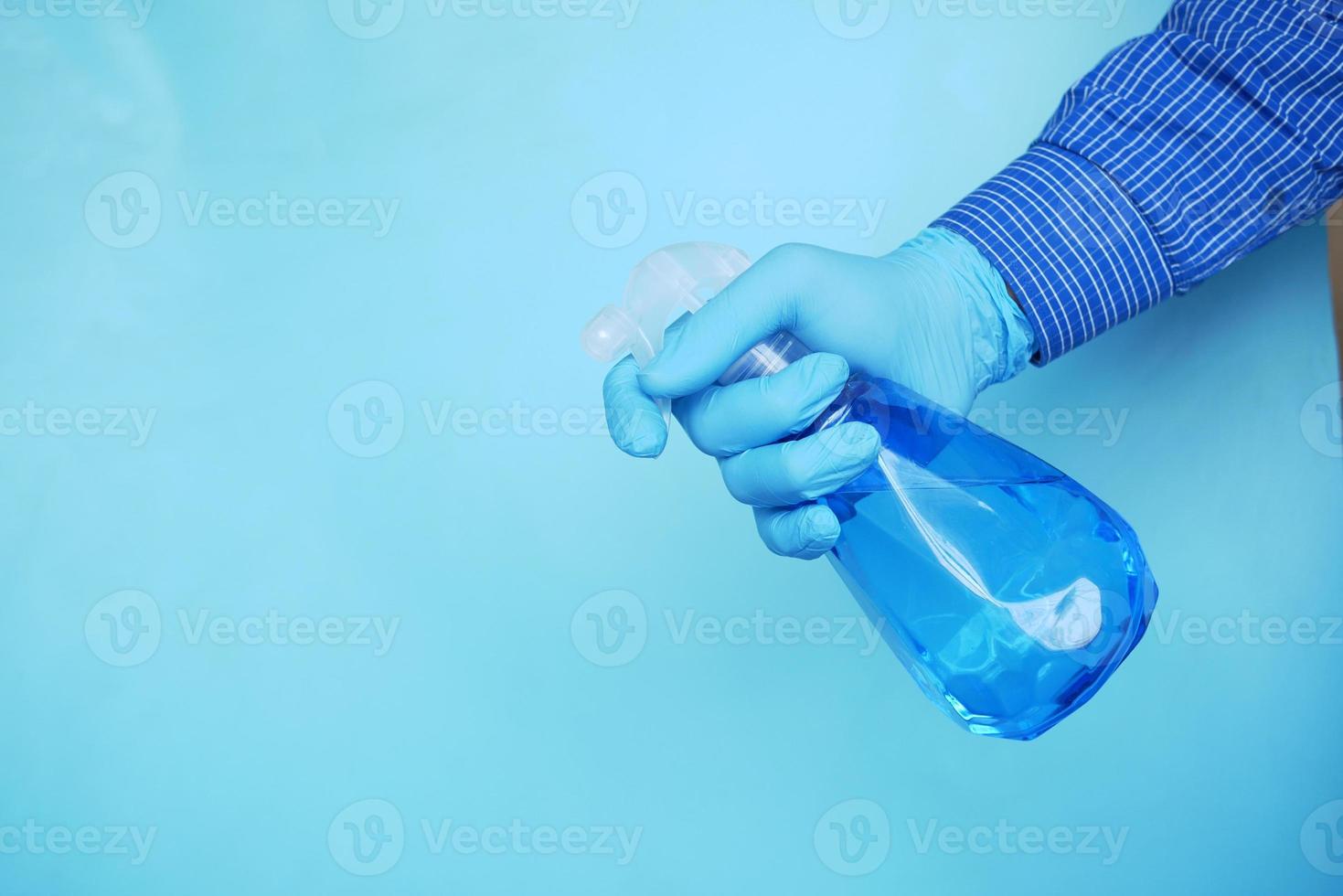 Hand in blue rubber gloves holding spray bottle with copy space photo