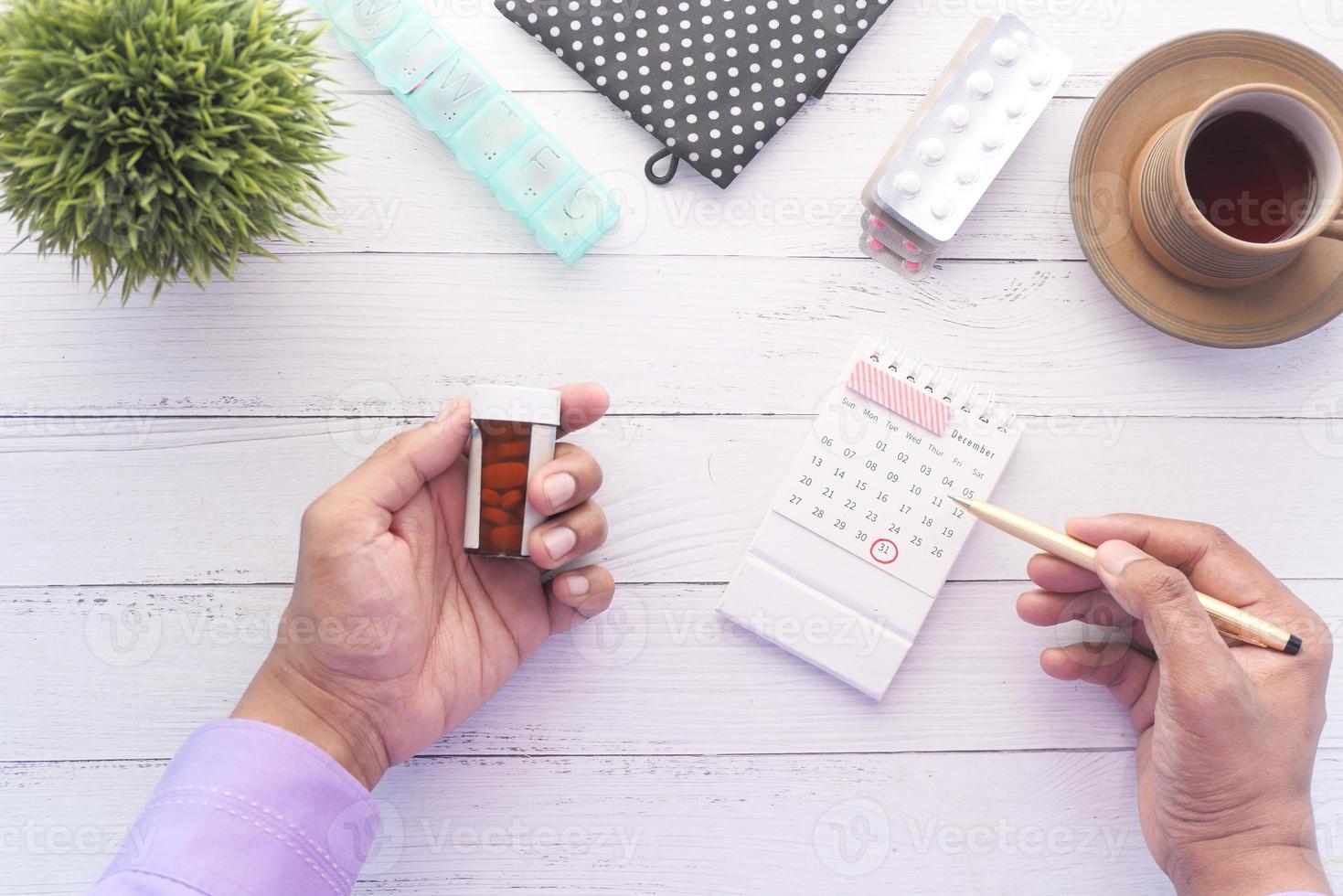 persona mano sujetando el contenedor de pastillas y el calendario foto