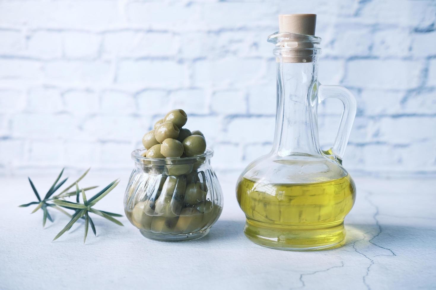 Bottle of olive oil and fresh olive in a container on wooden table photo