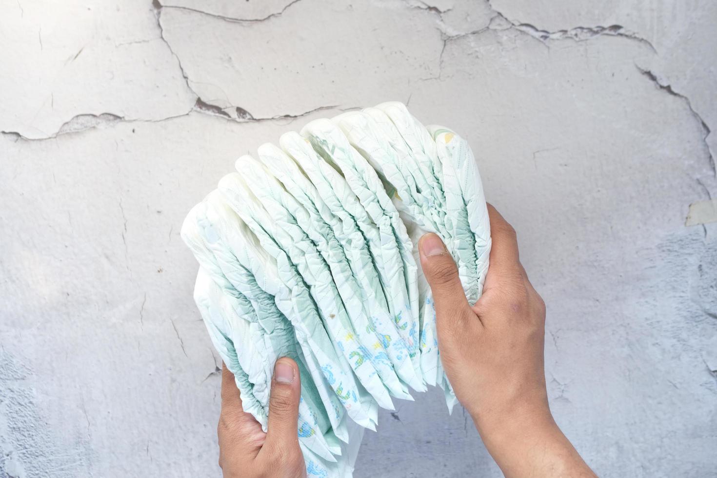 Hand holding stack of baby diaper on table photo